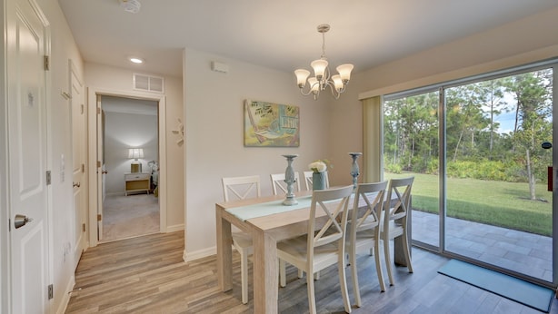 A dining area with a wooden table and chairs, a chandelier, and a view of the outdoors. - Gulf Cost Home 5min to I-75 & Sunseekers Resort (Port Charlotte)