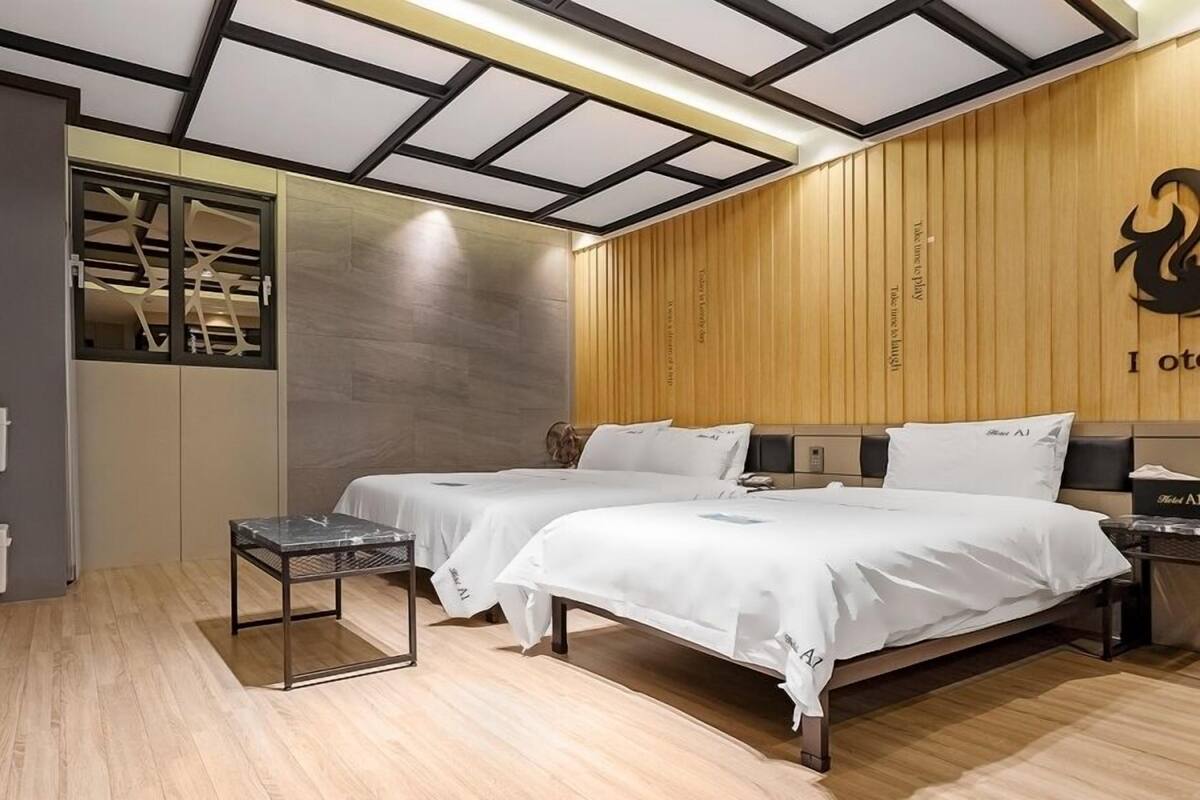Habitación de hotel con dos camas, un panel de pared de madera, techo con diseños geométricos y una pequeña mesa.