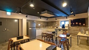 Una cocina moderna con horno empotrado, microondas y cafetera. Hay mesas y sillas de madera, y un ventanal que proporciona luz natural.