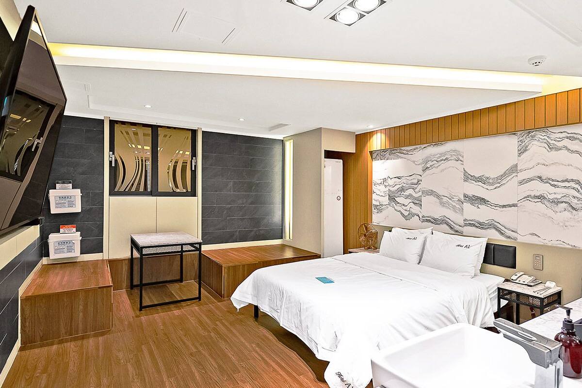 Habitación de hotel moderna con una cama grande, un banco de madera, un escritorio y una obra de arte grande en la pared.