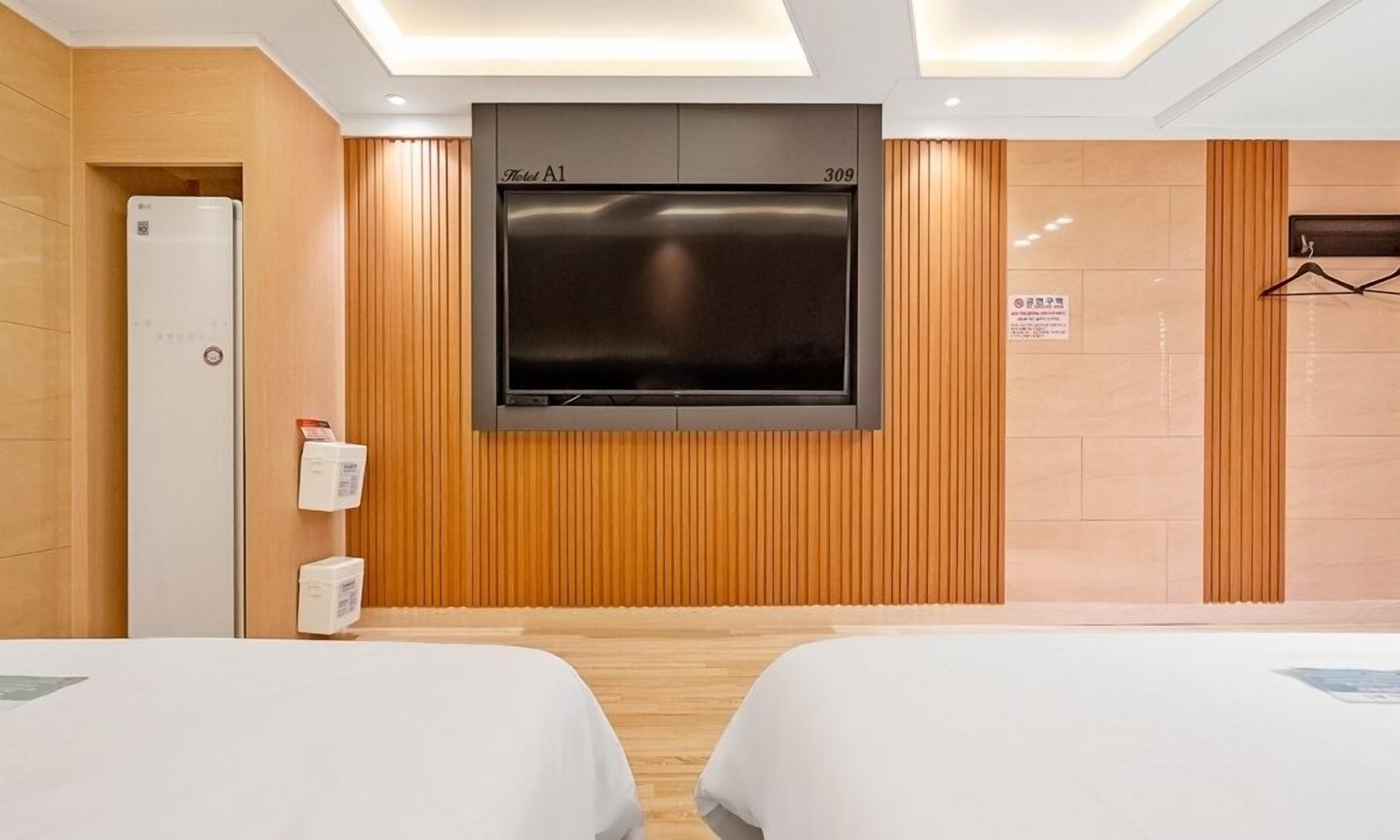 A hotel room with two beds, a TV mounted on the wall, a minibar, and a wooden panel wall.