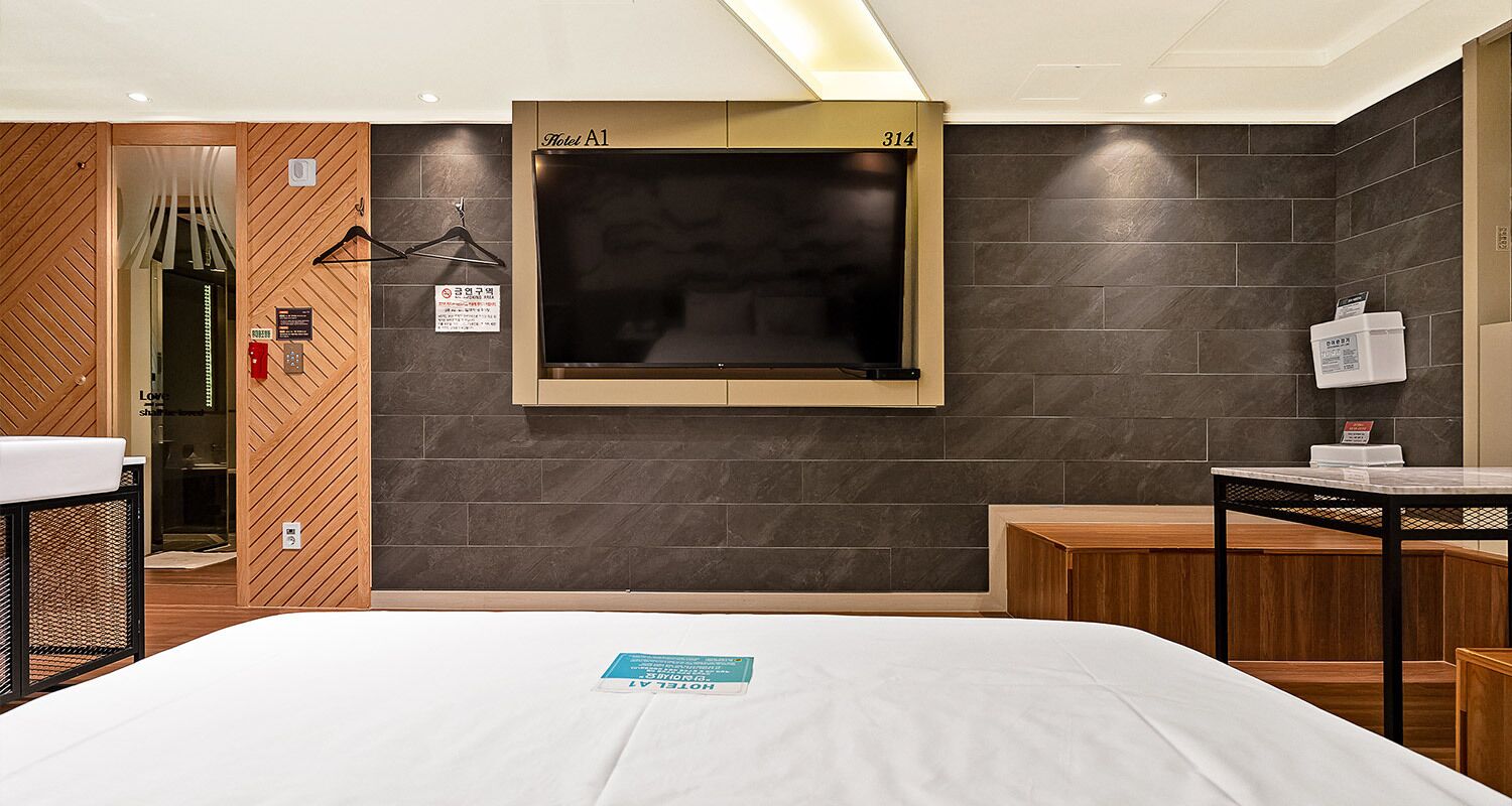 Een hotelkamer met een bed, nachtkastje, een aan de muur bevestigde televisie en een houten garderobe.