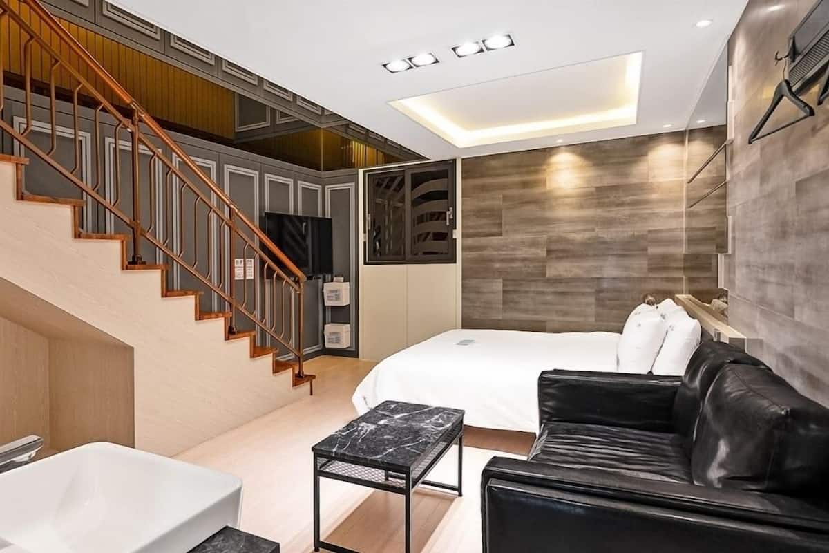 Una habitación de hotel moderna con una escalera, una cama, un sofá de cuero negro, una mesa con cubierta de mármol y una bañera.