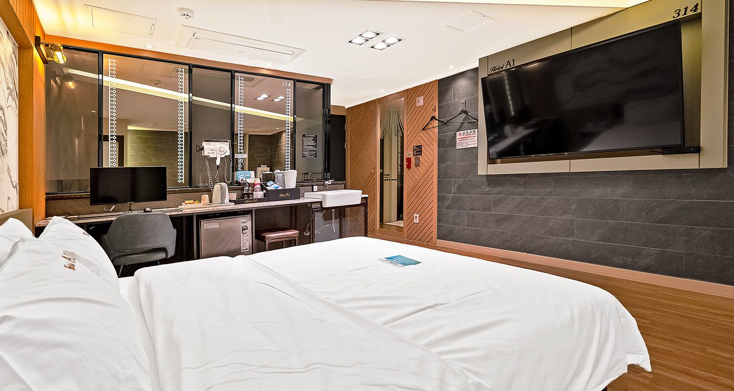 Een hotelkamer met een bed, een bureau met een computer, een spiegel en een televisie aan de muur.