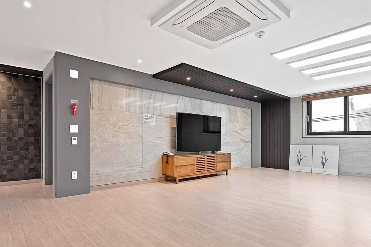 Habitación de hotel moderna con un televisor grande, mueble de madera, pared de mármol y una ventana con una obra de arte.
