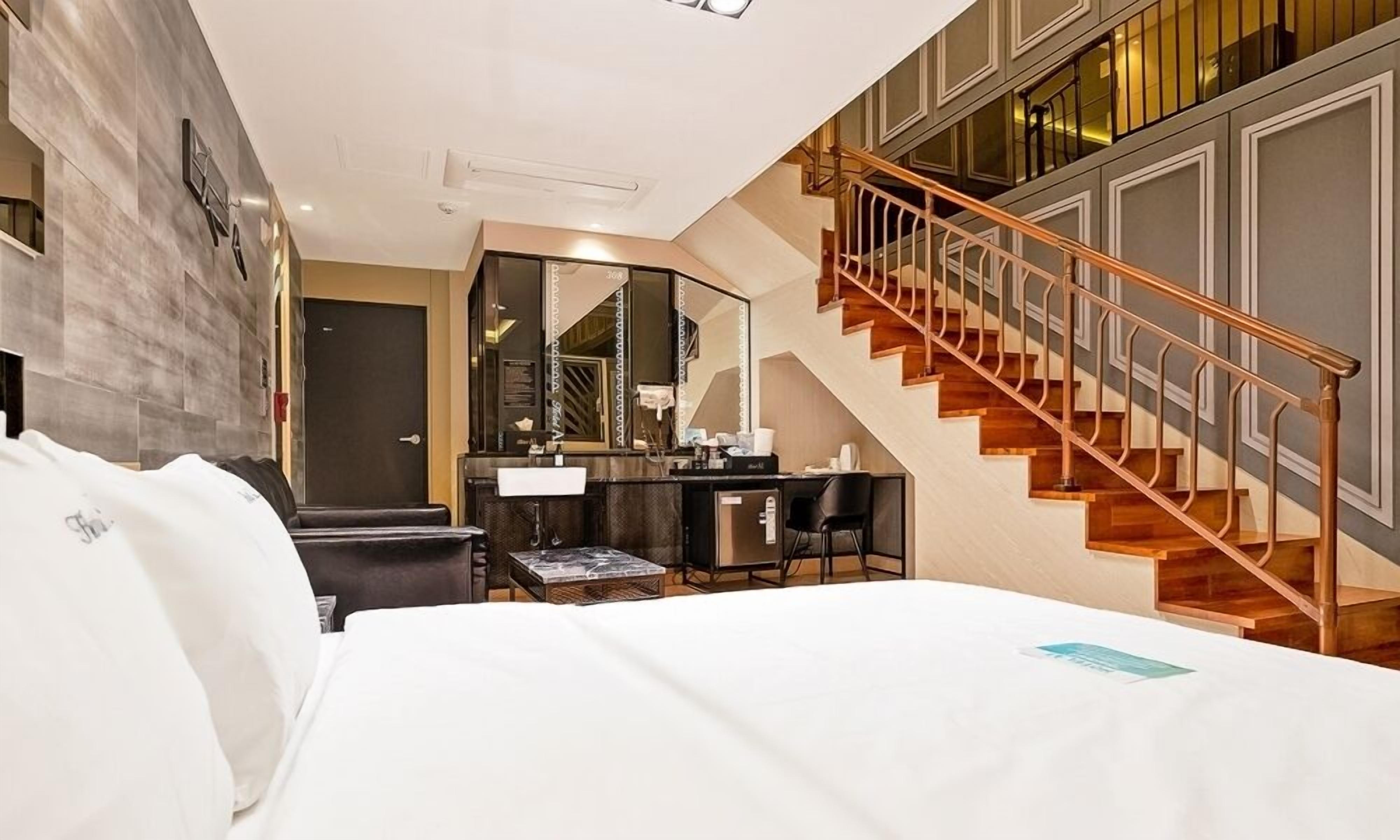 Ein Hotelzimmer mit einem großen Bett, einem Schreibtisch mit Spiegel, einem kleinen Tisch und einer Treppe.