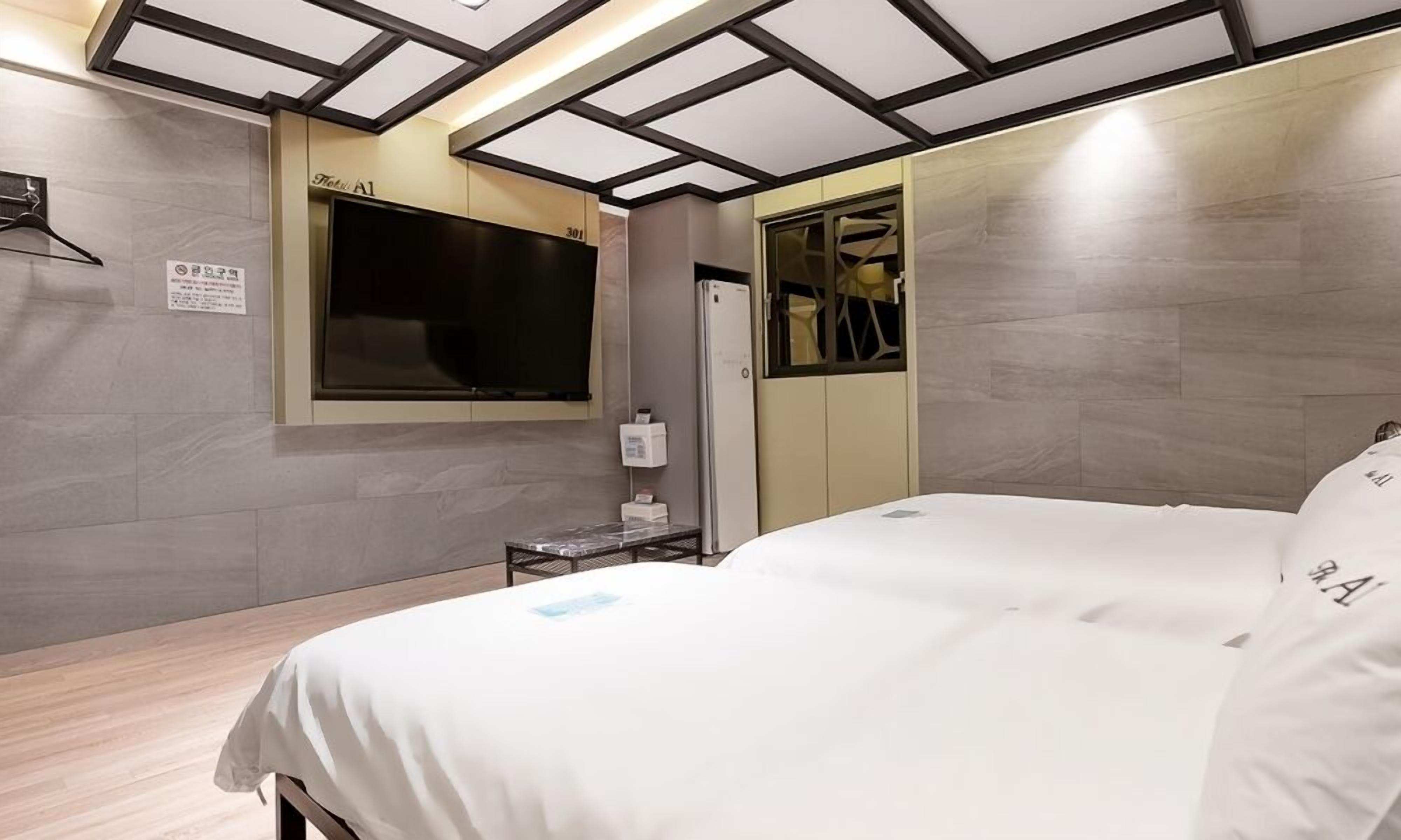 Een hotelkamer met een bed, een aan de muur bevestigde televisie, een spiegel en een tafeltje met een fles.