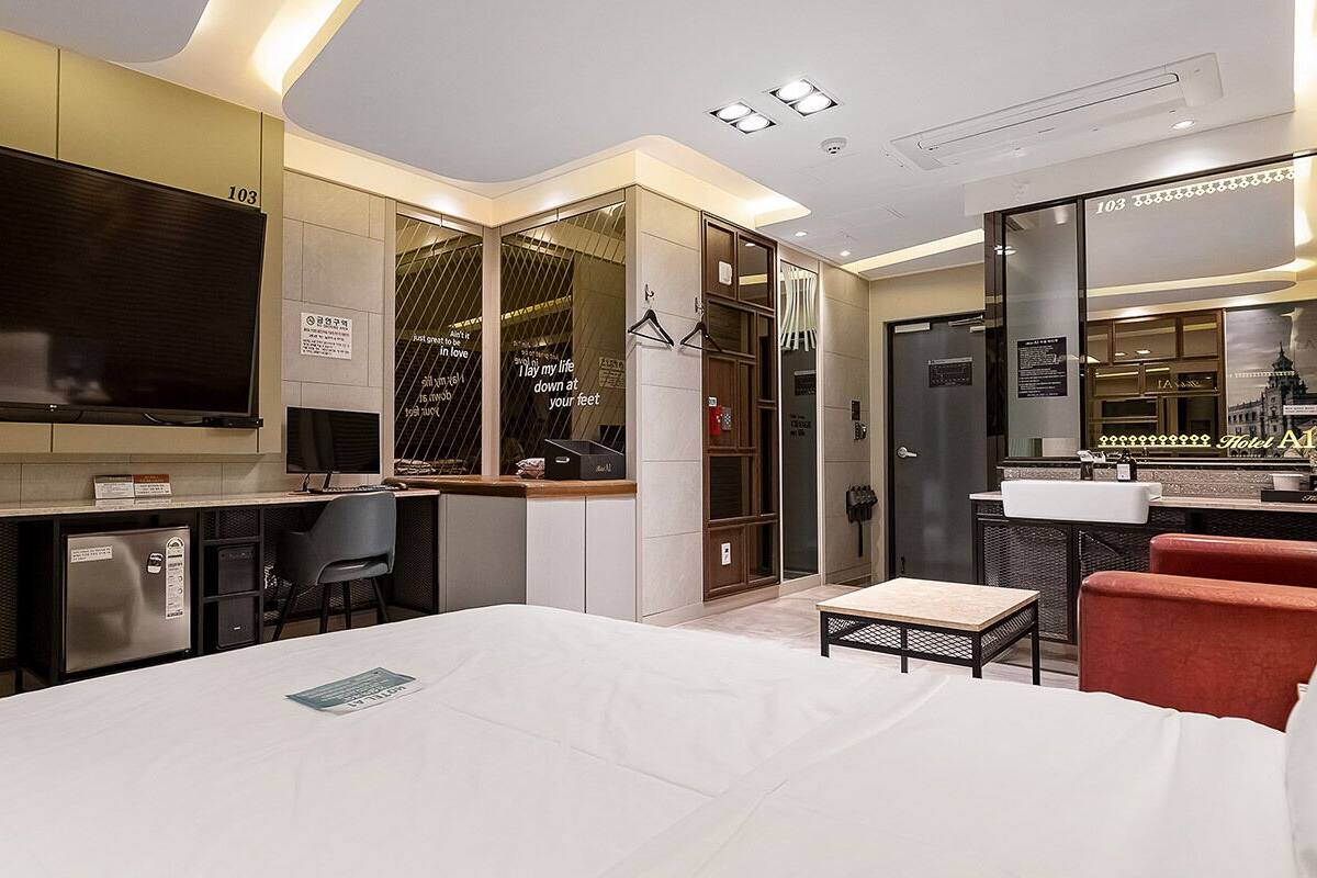 Una habitación de hotel moderna con una cama grande, un escritorio con computadora, un televisor y un mini bar.