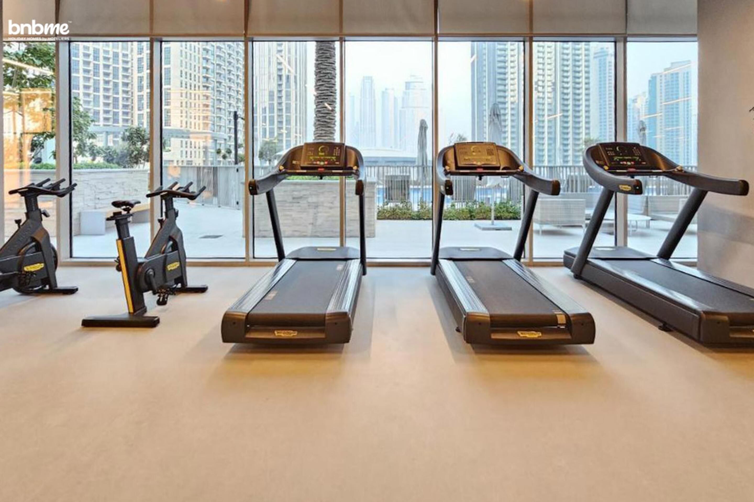 A gym with treadmills and stationary bikes, large windows with a city view.