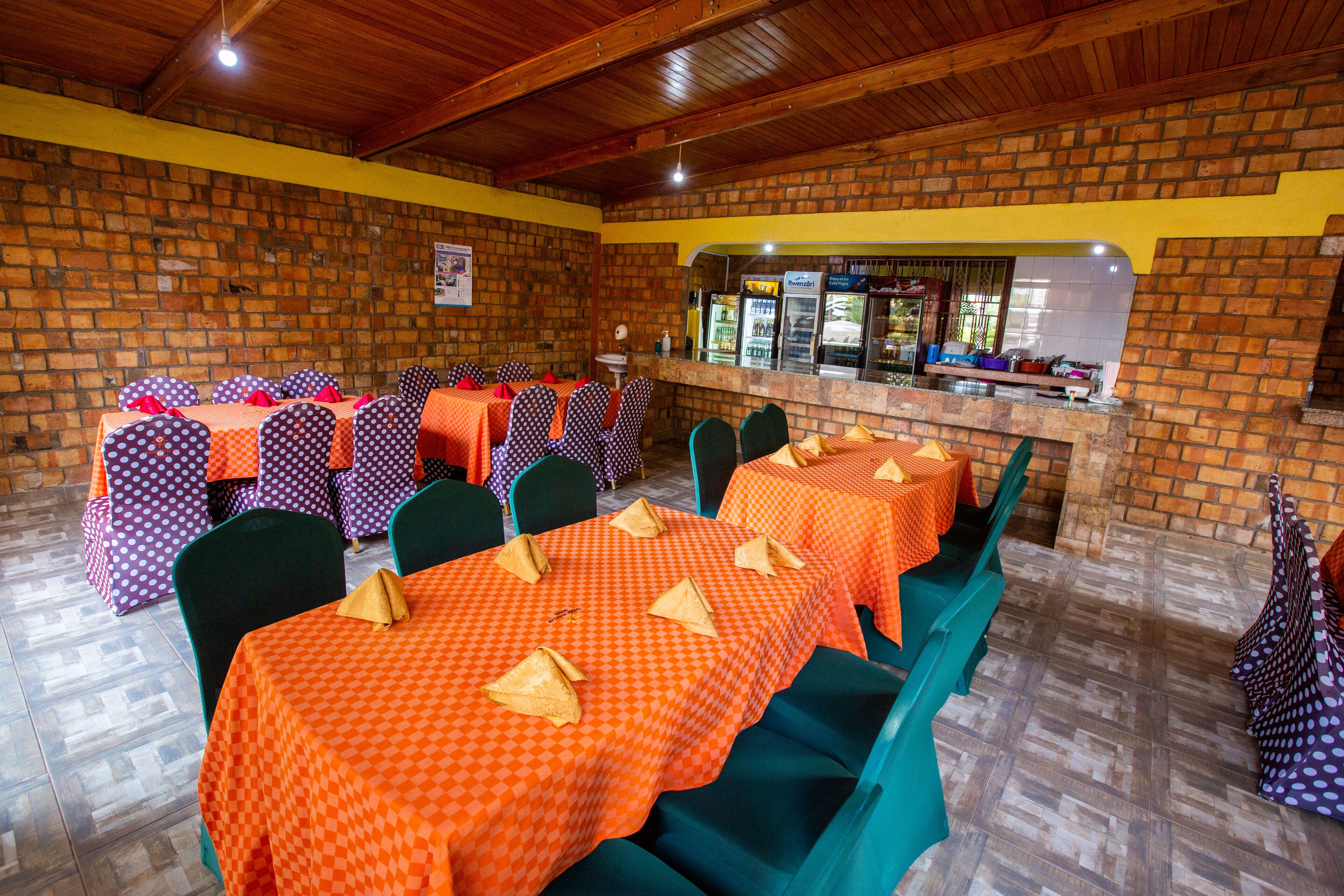 Un restaurante con paredes de ladrillo, mesas con manteles a cuadros anaranjados y sillas verdes.