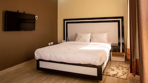 Een net opgemaakt bed met witte lakens, een zwart hoofdbord en een klein nachtkastje met een lamp.