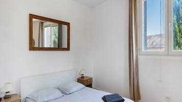 A bedroom with a bed, a nightstand, a lamp, a mirror, and a window with curtains.
