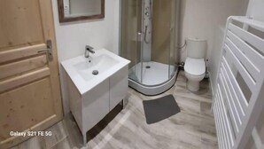 Un baño con ducha envuelta en vidrio, un lavamanos blanco y un inodoro.