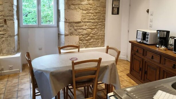Un comedor con pared de piedra, ventana con vista a follaje, una mesa con sillas y una zona de cocina con electrodomésticos.
