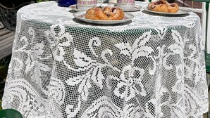 Une table dressée à l’extérieur, avec une nappe en dentelle, un service à thé et des pâtisseries.