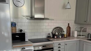 Une cuisine moderne avec des meubles blancs, une hotte de cuisinière en acier inoxydable, un four encastré, un four à micro-ondes et une horloge murale.