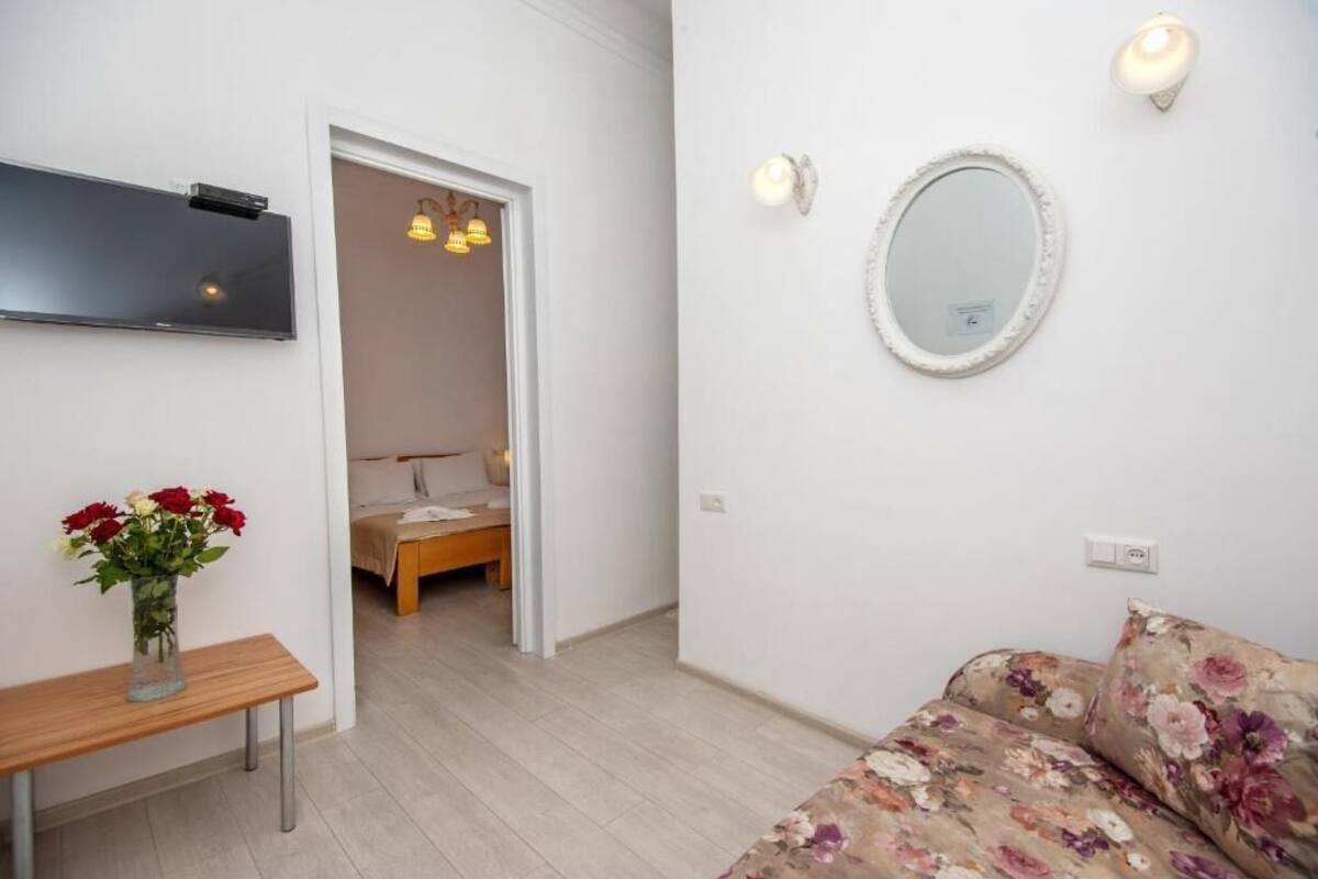A bedroom with a bed, a bedside table with a vase of flowers, a wall-mounted TV, and a mirror.
