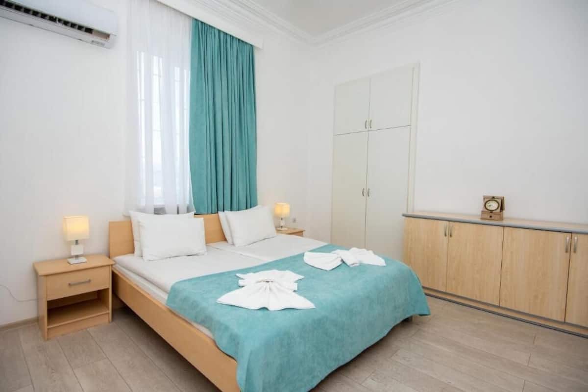 A hotel room with a bed, two bedside tables, a wardrobe, and a window with curtains.