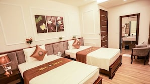 A hotel room with two beds, each with a brown bedspread and a pillow with a logo. There is a nightstand with a lamp, a chair, and a mirror. The room has a wooden floor and white walls. - Sen Hotel by Bay Luxury (Hanoi)