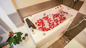 A bathtub filled with rose petals, a shower, and a potted plant. - Sen Hotel by Bay Luxury (Hanoi)
