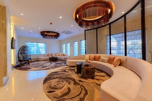 A modern living room with a curved sofa, a patterned rug, and a unique ceiling light fixture. - Four A Resort Jammu (Samba)