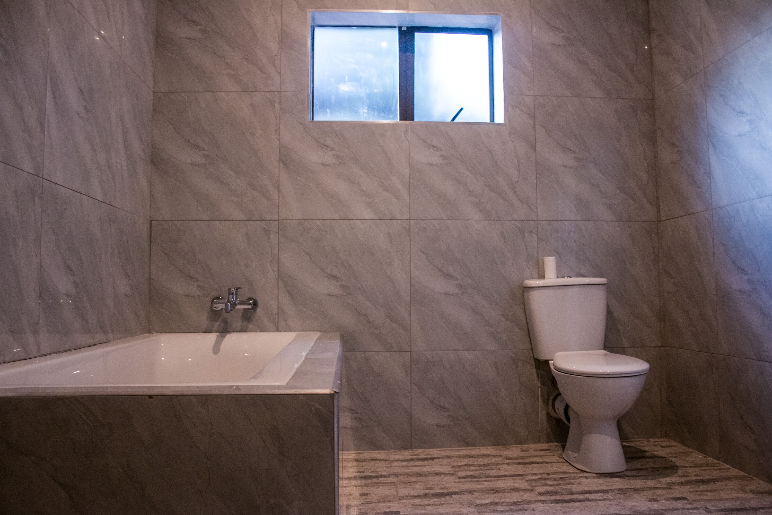 A bathroom with a bathtub, toilet, and a small window.