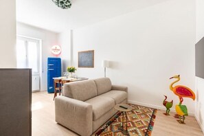 Una sala de estar con un sofá, una mesita redonda, un tapete colorido y un aparador azul.