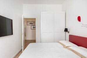 Un dormitorio con una cama, un televisor en la pared, una puerta y una lámpara de pared.