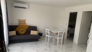 A living room with a dark sofa, patterned cushions, a small table, and chairs. - Loue Appartement T2 Lozari (Palasca)