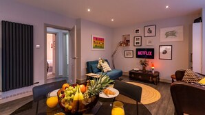 Ein modernes Wohnzimmer mit Essbereich, ausgestattet mit Obstschale, Sofa, Fernseher und gerahmten Kunstwerken an der Wand.