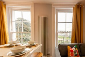 A dining area with a table set for two, a radiator, and a sofa with a colorful pillow.