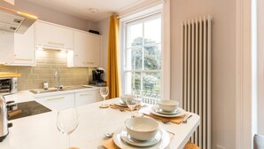 Een moderne keuken met witte kastjes, een ingebouwde oven en een groot raam met gele gordijnen.