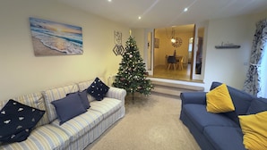 Una sala de estar con un sofá a rayas, un sofá azul con almohadones amarillos, un árbol de Navidad y un cuadro de una playa.