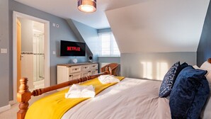 Un dormitorio con cama, televisor montado en la pared, cabecera de madera y ventana con persianas.