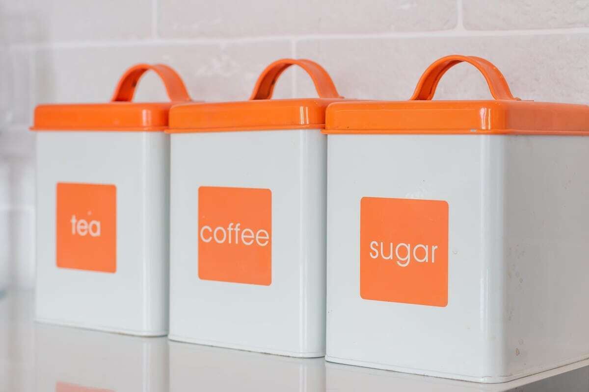 Three white containers with orange lids and handles, labeled "tea," "coffee," and "sugar."