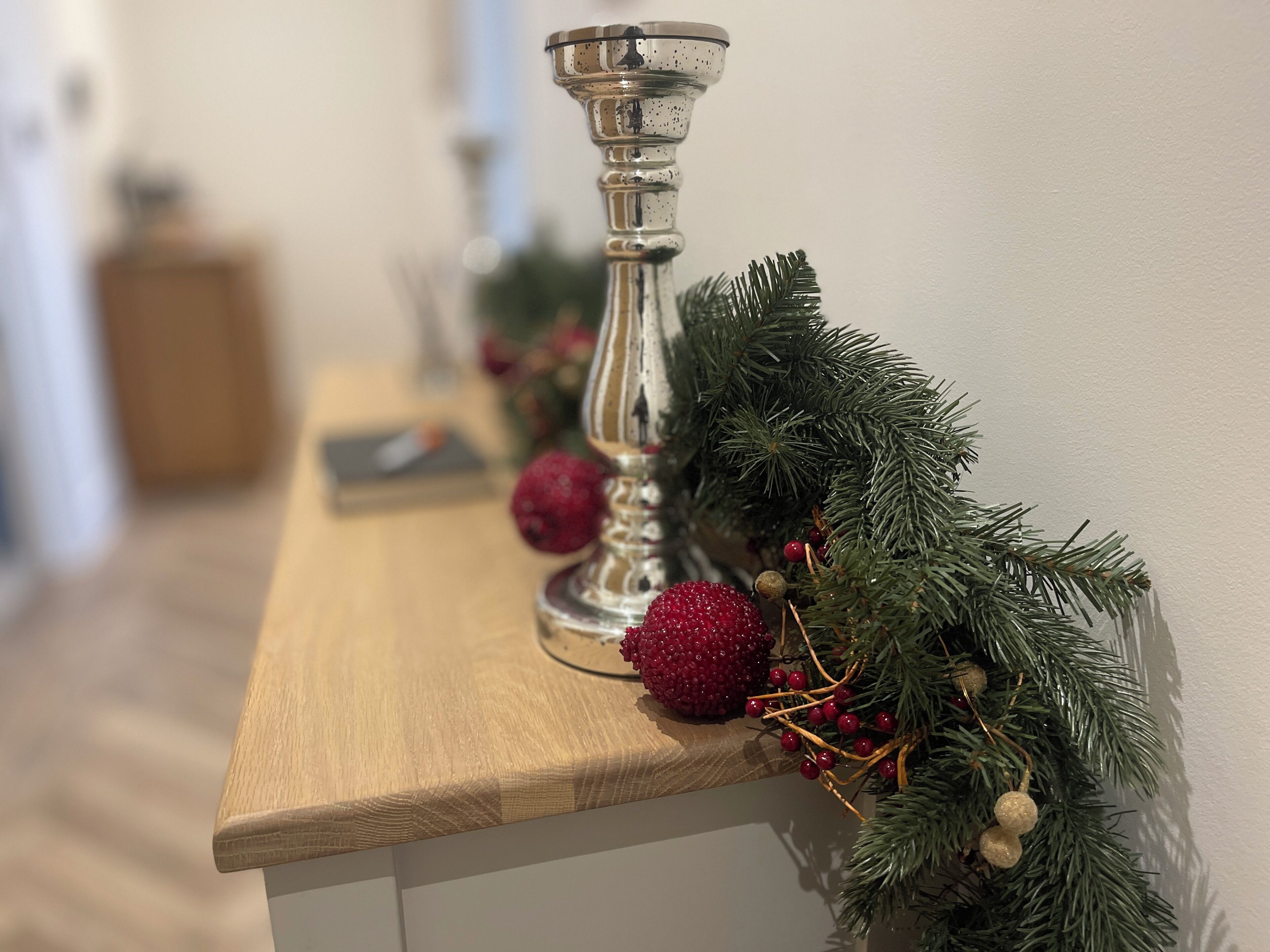 A wooden table with a silver candle holder and a garland with pine branches and red berries.