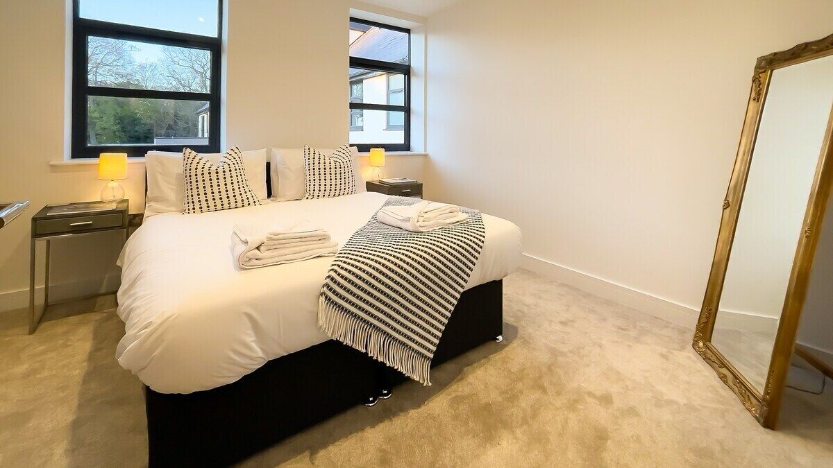 A neatly made bed with a striped blanket, two bedside lamps, and a large mirror on the wall.