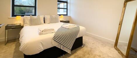 A neatly made bed with a striped blanket, two bedside lamps, and a large mirror on the wall.