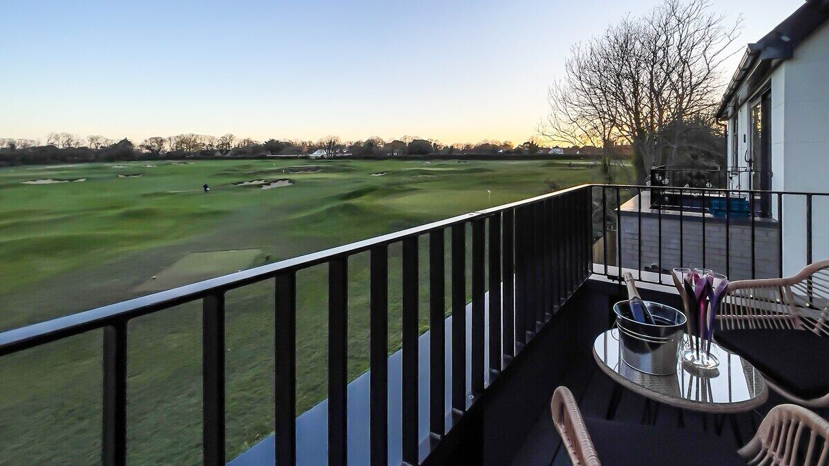 A balcony with a view of a golf course, a table with chairs, and a barbecue grill.