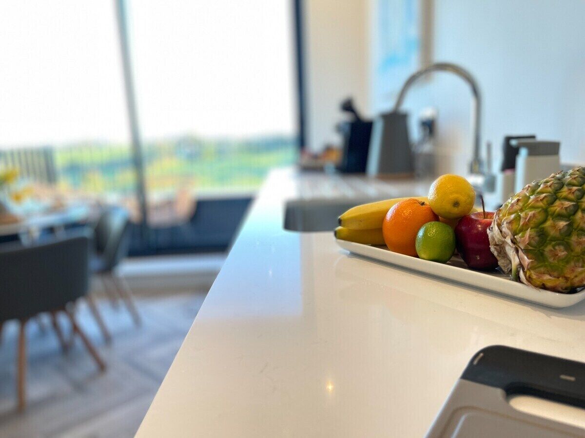 A kitchen counter with a fruit bowl containing bananas, oranges, and a pineapple.