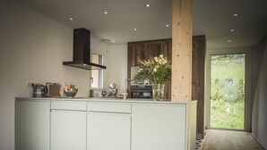 A modern kitchen with a central island, wooden accents, and a view of greenery outside.