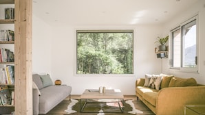 A modern living room with a large window, a bookshelf, a grey sofa, a yellow sofa, and a glass coffee table.