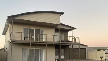 Two-story residential building with a flat roof and curved design element, featuring large windows and a covered balcony.