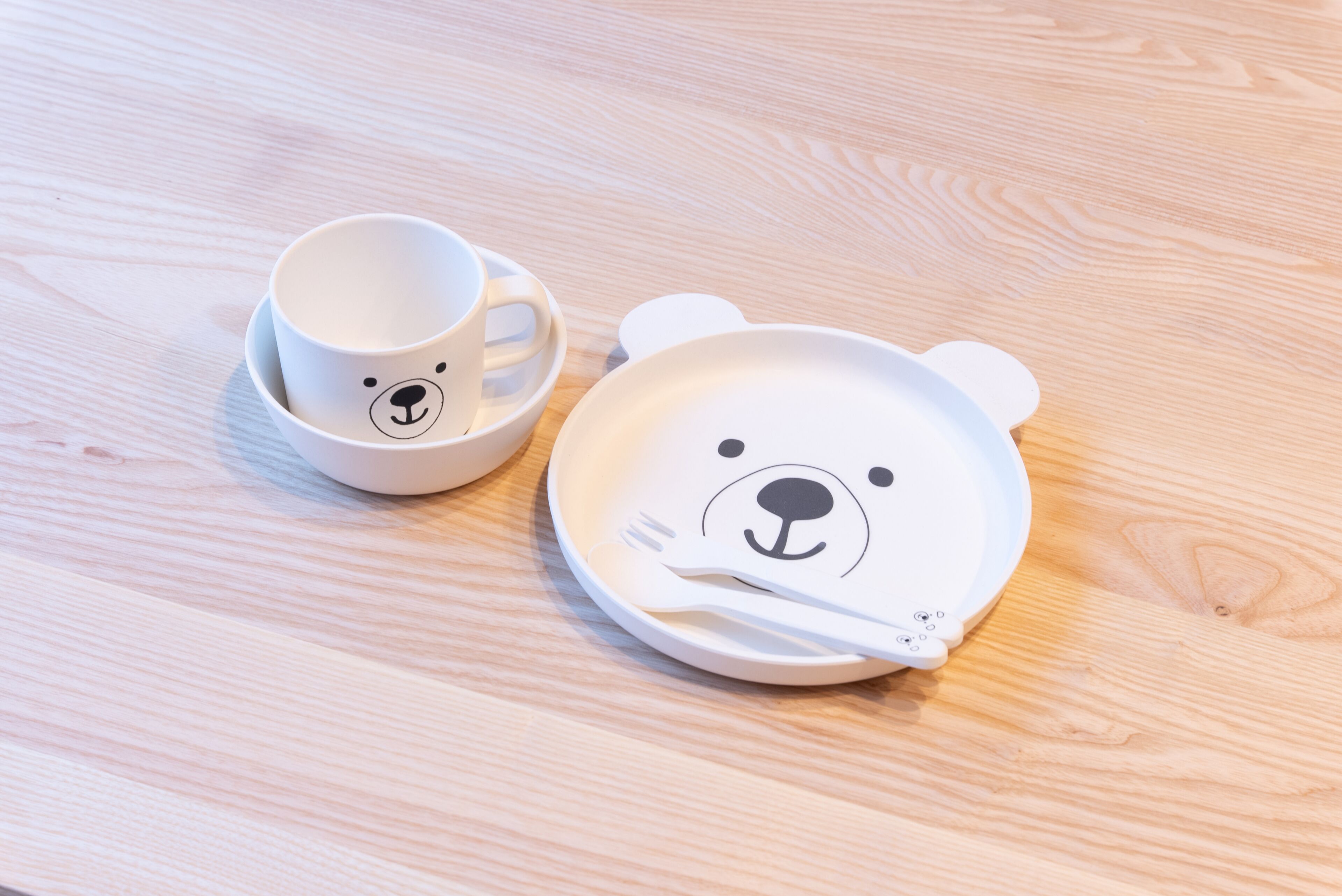 Una mesa de madera con un plato y una taza blancos con forma de oso.
