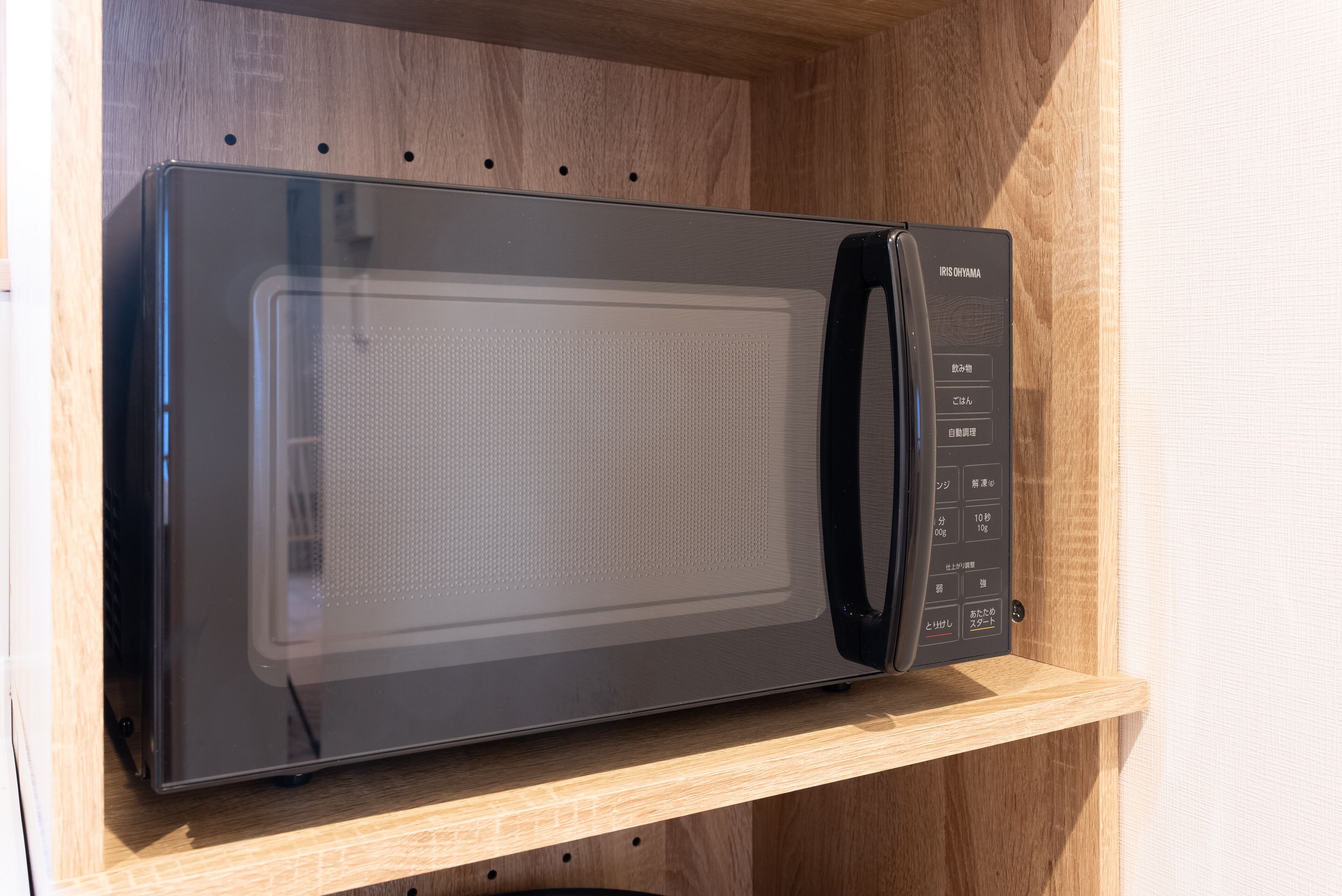Un four à micro-ondes noir doté d’un panneau de commande numérique, posé sur une étagère en bois.
