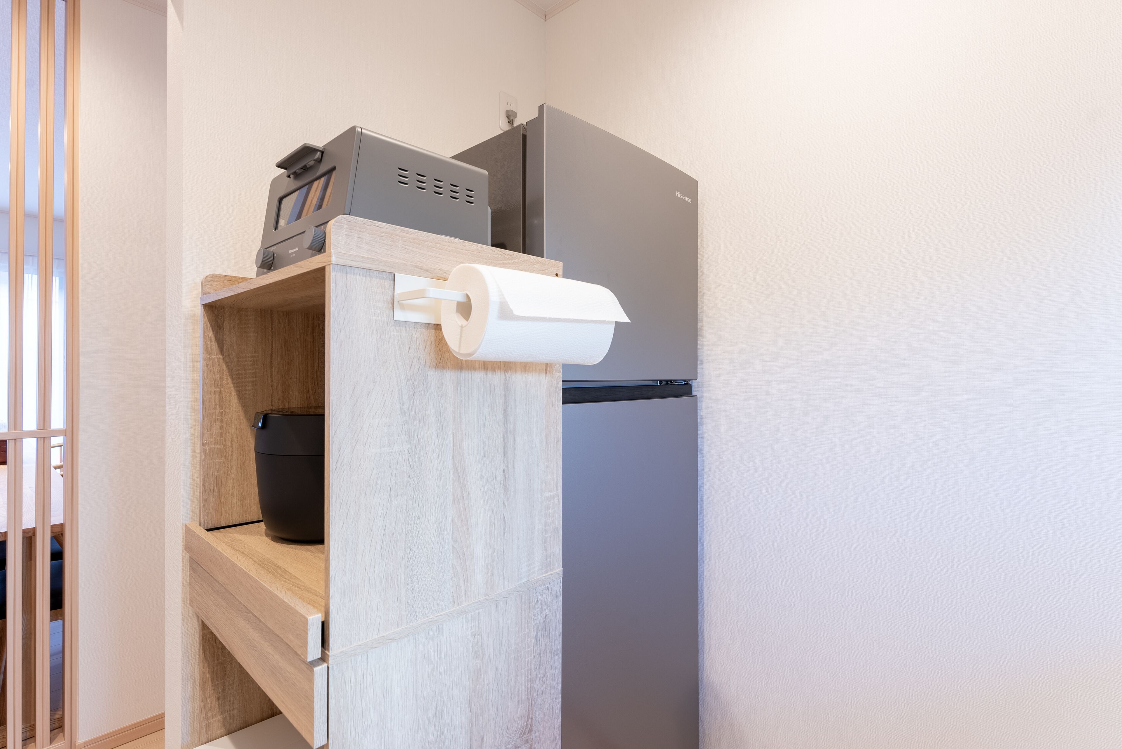 A compact kitchen with a built-in refrigerator, a microwave, and a wooden shelf with a black container.