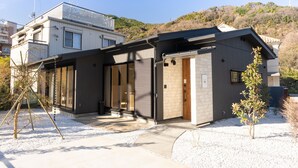A modern two-story house with a covered porch, large windows, and a small garden area. - Stagione Hakone Yumoto Villa (Hakone)