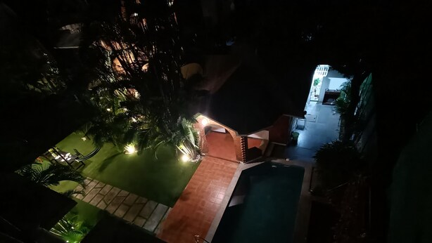 Una vista nocturna de un patio con piscina, zona de comedor y área de estar cubierta.