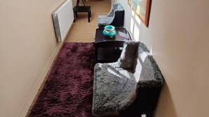 A narrow hallway with a sloped ceiling, a purple rug, a gray sofa, a small table with a teal vase, and a framed picture on the wall. - Un Appartement Dans un Château (Deauville)