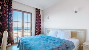A bedroom with a bed, a nightstand, a chair, a window with curtains, and a view of the sea. - Miletus Otel (Sile)